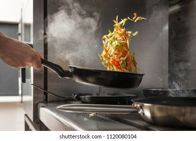 Chef Tossing Vegetables On Frying Pan At Professional Kitchen. 