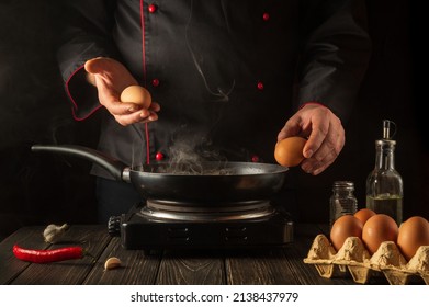 The Chef Tries To Break An Egg On A Frying Pan To Make Delicious Breakfast. Working Environment In The Kitchen. Menu Idea For A Restaurant Or Hotel.