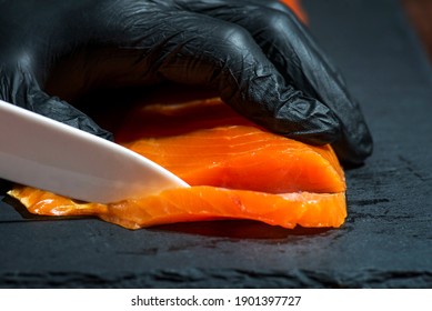 Chef use knife to cutting salmon fillet on black board at professional kitchen. Closeup chef hands in black gloves slicing red fish slice. - Powered by Shutterstock