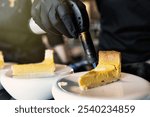 A chef uses a blowtorch to caramelize lemon tart slices on white plates. precision and culinary artistry, showing professional dessert preparation in a restaurant