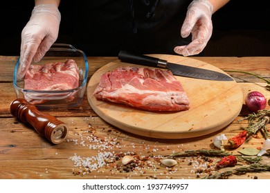 The chef uses his hands to slice pork ribs with a knife on a wooden cutting table. Selective focus. The concept of the cooking process.