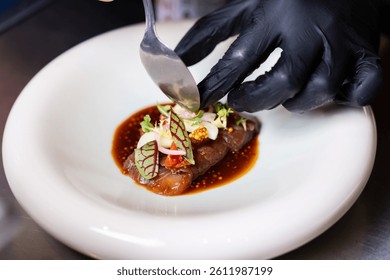 Chef using fork and knife to adjust garnish on gourmet beef in a fine dining setting.