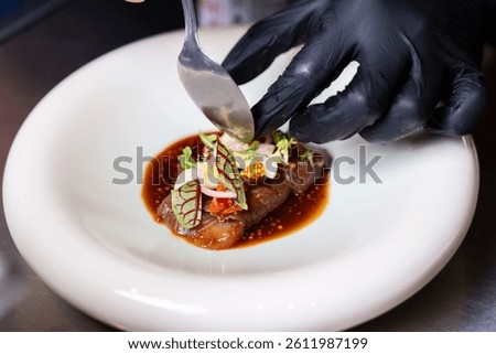 Chef using fork and knife to adjust garnish on gourmet beef in a fine dining setting.