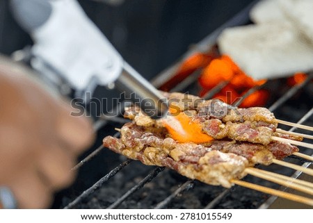 Chef using a kitchen torch to sear meat skewers on a charcoal grill