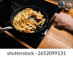 Chef is using spatula to turn batch of golden french fries cooking in non stick pan on modern cooktop, ensuring even browning and crispy texture. Chef turning golden french fries in non stick pan. POV