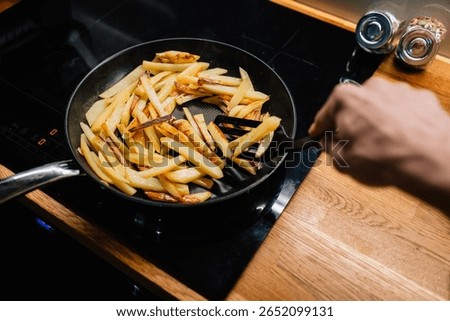 Chef is using spatula to turn batch of golden french fries cooking in non stick pan on modern cooktop, ensuring even browning and crispy texture. Chef turning golden french fries in non stick pan. POV