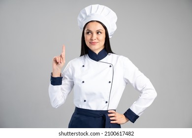 Chef mujer con uniforme y gorra sobre fondo gris aislado y apuntando con el dedo. Concepto de ocupación