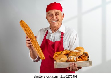 Chef-cooker In A Chef's Hat And Apron Working In Bakery, Holding Tray With Bread And Rolls. Senior Professional Baker Man Wearing A Chef's Outfit. Character Kitchener, Pastry Chef For Advertising.