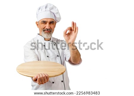 Chef-cooker in a chef's hat and jacket gesturing okay, holding an empty wooden tray for mock up. Senior professional baker man wearing a chef's outfit. Character kitchener, pastry chef for advertising