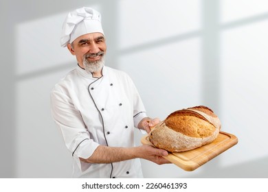 Chef-cooker in chef's hat and jacket working in bakery, holding French bread board with bread. Senior professional baker man wearing chef's outfit. Character kitchener, pastry chef for advertising.