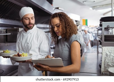 Chefs discussing menu on clipboard in commercial kitchen