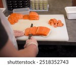 The chefs gloved hands move gracefully as he cuts fresh salmon into even pieces His special knife glides through the salmon, ensuring that each slice of salmon is perfectly even.