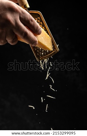The chef's hand rubs Parmesan on a grater freezing motion flying in the air on a dark background, vertical image. place for text,