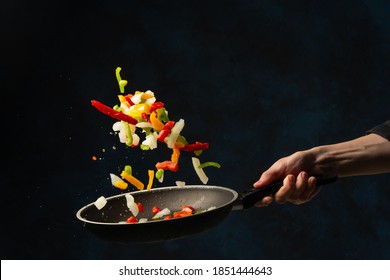 Chef's hand throws up frying mix of colored vegetables above the pan on dark blue background. Backstage of cooking meal. Frozen motion. Food banner concept. - Powered by Shutterstock