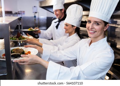 Chefs handing dinner plates through order station in the kitchen - Powered by Shutterstock