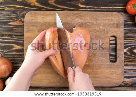 Chef's hands cut chicken fillet top view