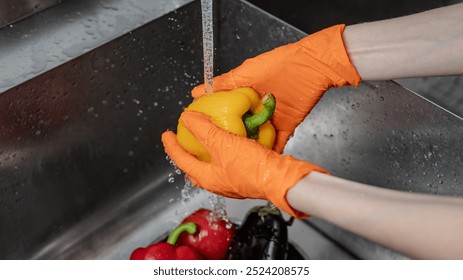 Chef's hands in orange gloves close-up washes bell peppers - Powered by Shutterstock