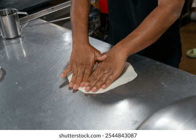 Chef's hands skillfully flatten dough on a metal surface, preparing for a delicious culinary creation. - Powered by Shutterstock