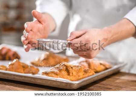 Chefs hands with small sieve over baking