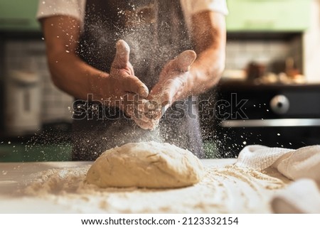 Chef's hands spraying flour over the dough. Kneading dough. Male chef in kitchen chef's apron spraying flour over dough