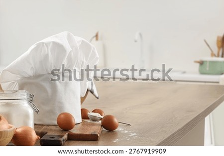 Chef's hat with cutting board, eggs and flour on table in kitchen