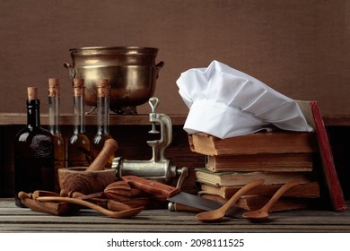 Chef's hat, vintage cookbooks, and old kitchen utensils on the wooden table. A conceptual image on the theme of culinary art.