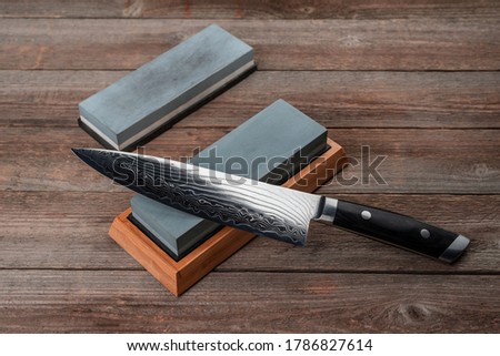 Chef's knife and whestones on rustic wooden background. Beautiful texture of Damascus steel and sharp blade.