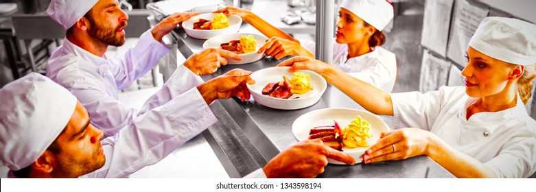 Chefs Passing Ready Food To Waiter At Order Station In Commercial Kitchen