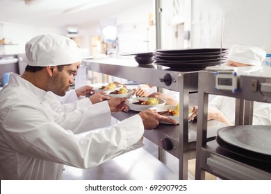 Chefs Passing Ready Food To Waiter  At Order Station In Commercial Kitchen