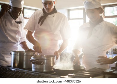 Chefs Preparing Food At Stove In Commercial Kitchen