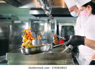 Chefs in protective masks and gloves prepare food in the kitchen of a restaurant or hotel - Powered by Shutterstock