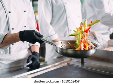 Chefs In Protective Masks And Gloves Prepare Food In The Kitchen Of A Restaurant Or Hotel