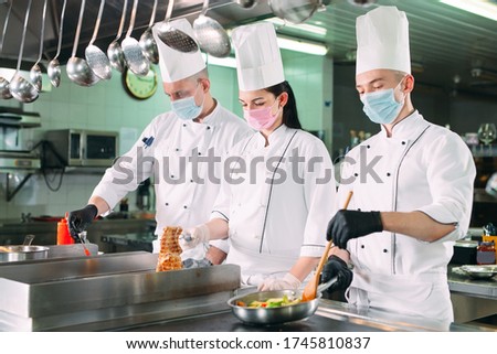 Chefs in protective masks and gloves prepare food in the kitchen of a restaurant or hotel