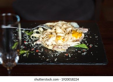 The Chef's Serving Is Pasta Carbonara With Poached Egg, Bacon And Herbs On A Dark Stone Platter. Close-up, Horizontal Orientation, Copy Space, No People