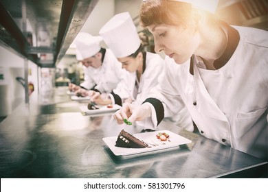 Chefs standing in a row garnishing dessert plates in the kitchen