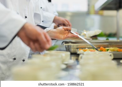 Chefs standing in a row preparing food in a modern kitchen - Powered by Shutterstock