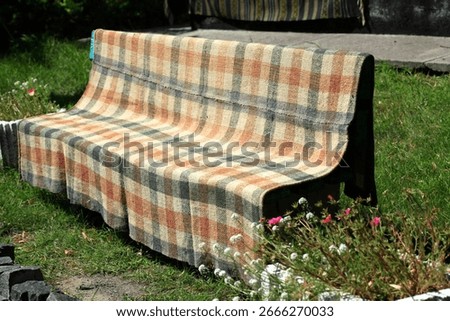 A chekered blanket is drying on a bench