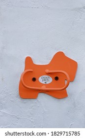 Cheltenham Gloucestershire UK October 7th 2020 Bright Orange Hook On The Shape Of A Dog Designed To Hold A Dog Lead Outside A Shop, Screwed Onto A White, Textured Wall - A Place To Park Your Dog!