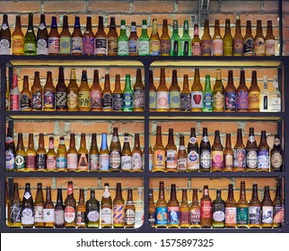 CHELYABINSK / RUSSIA - NOVEMBER 27, 2019: Various Types Of Craft Beer Bottles Display On Shelf At Bar. Alcohol Drink Different Import Beer Style Microbrews. Rustic Brick Wall Interior.