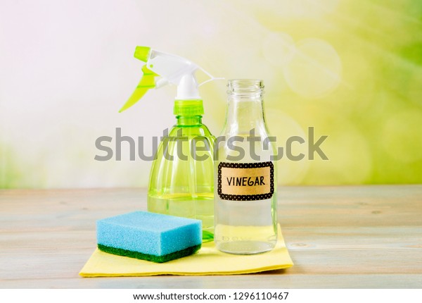 Chemical free home\
cleaner products concept. Using natural destilled white vinegar in\
spray bottle to remove stains. Tools on wooden table, green bokeh\
background, copy\
space.