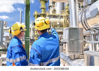 Chemical Industry Plant - Workers In Work Clothes In A Refinery With Pipes And Machinery 