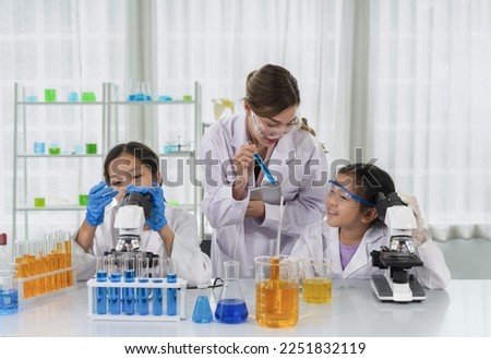 chemical laboratory staff as a mentor teaching kids in science classroom, young female hand holding tablet and other hand showing liquid tube and talking to a little kid 