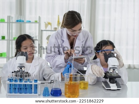chemical laboratory staff as a mentor teaching kids in science classroom, young female hand using tablet while teaching a little kid 