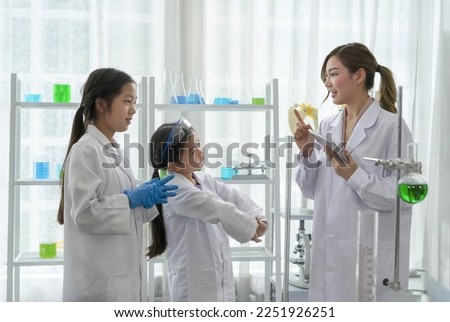 chemical laboratory staff as a mentor teaching kids in science classroom, young female hand holding tablet talking to a little kids