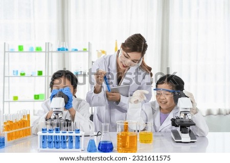 chemical laboratory staff as a mentor teaching kids in science classroom, young female hand holding test tube and other hand holding  tablet while teaching a little kid 