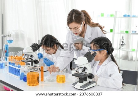 chemical laboratory staff as a mentor teaching kids in science classroom, young female hand holding experiment slide and other hand holding  tablet while teaching a little kid 