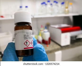 Chemical Reagent In An Amber Bottle In A Scientific Research Laboratory. Attention Or Danger Symbol On The Label. Background Of Equipment And Lab Glassware.