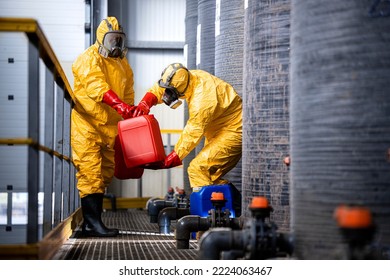 Chemical worker carrying canisters with hazardous materials and standing by large storage acid tanks. - Shutterstock ID 2224063467