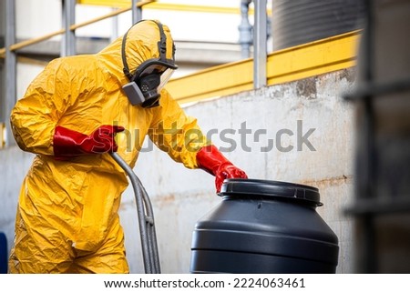 Chemical worker in protective suit and gas mask working with hazardous materials and toxic waste in production plant.