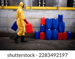 Chemical worker in yellow protection suit and gas mask working in factory carrying canisters dangerous material.